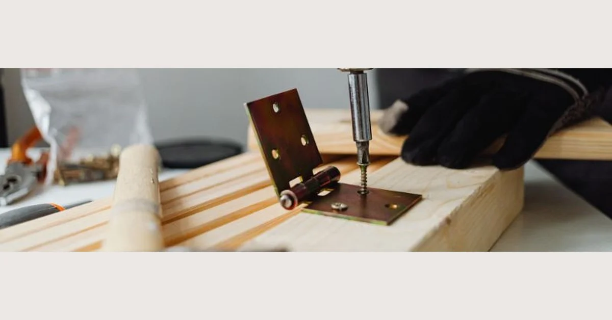 Drilling a screw into a door hinge on a wood panel closeup