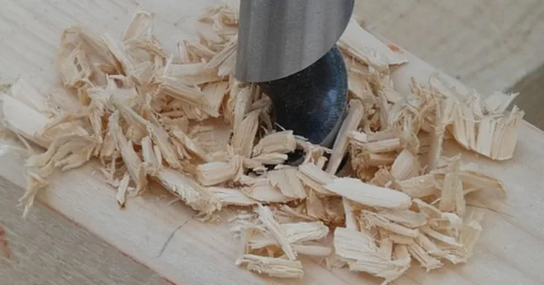 Auger drill bit boring a hole through a wood board with wood chips