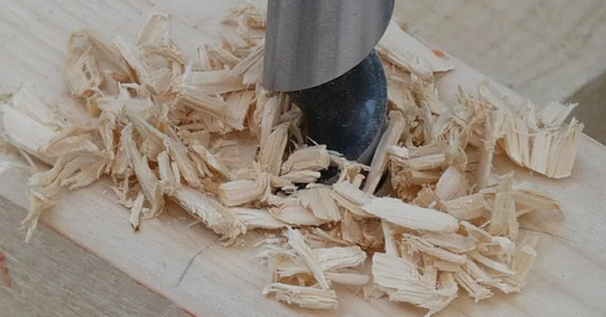 Auger drill bit boring a hole through a wood board with wood chips