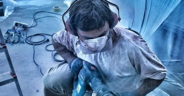 Worker drilling into a concrete slab with an SDS rotary hammer drill and safety gear