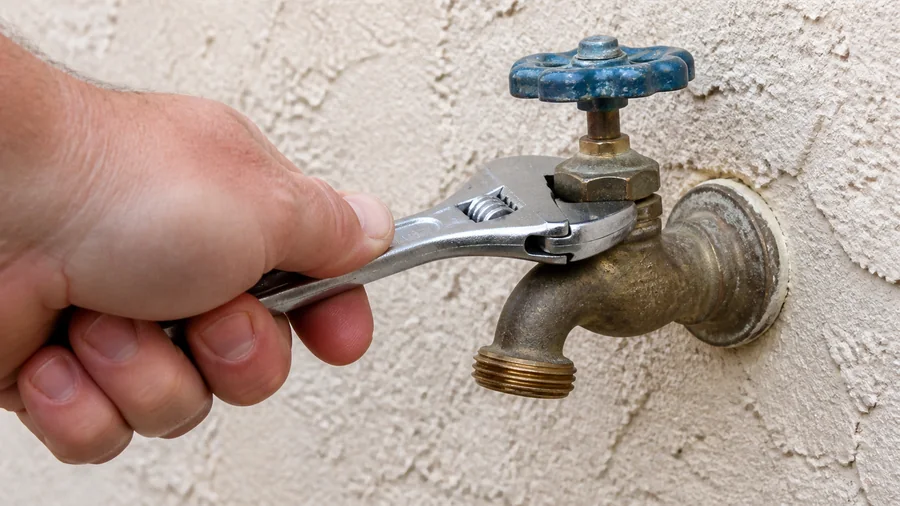 Outdoor hose faucet being checked for a drip at the spout and hose connection