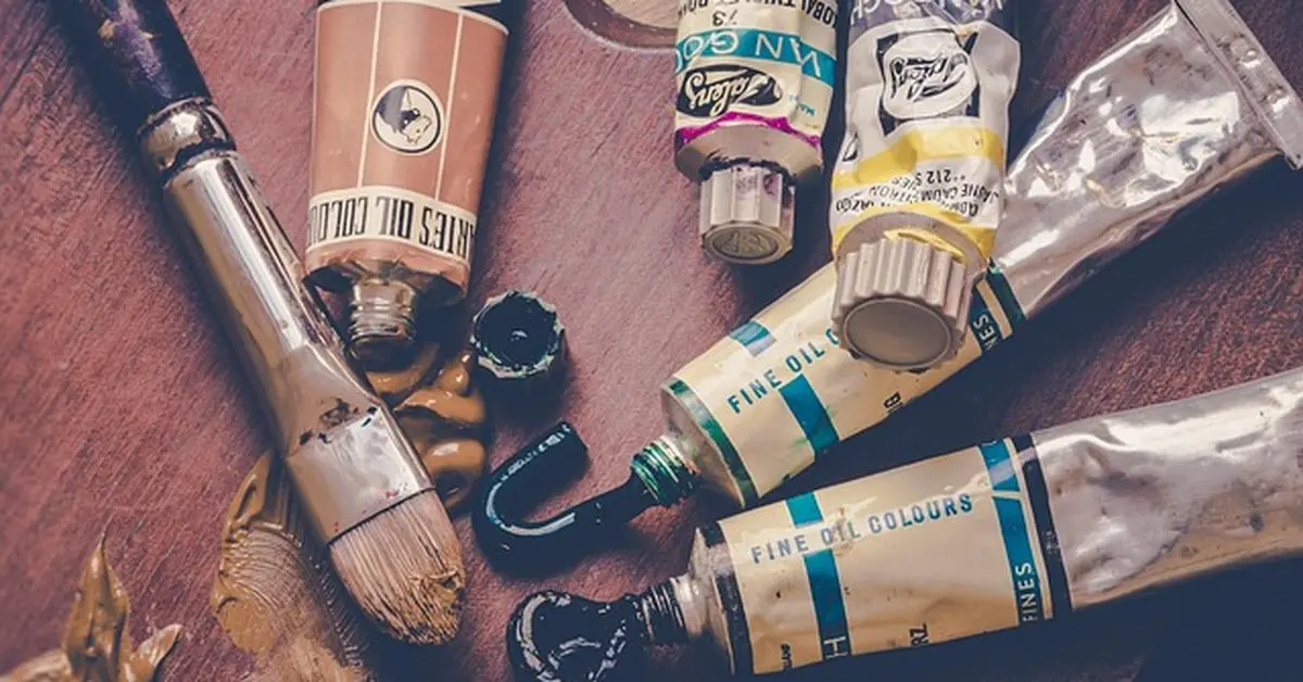 Paint tubes and brush with wet paint on a wooden surface