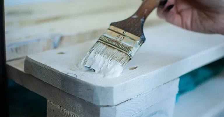 Hand painting white paint onto wood furniture with a brush