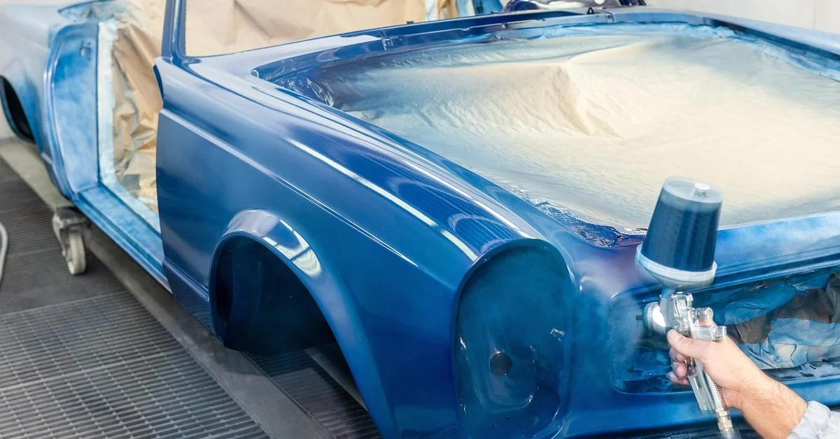 Technician spraying Plasti Dip rubber coating onto a car body panel with a spray gun