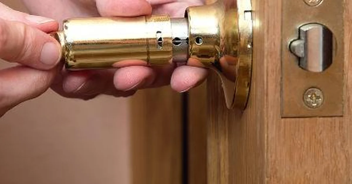 Hands removing a deadbolt lock cylinder from a door
