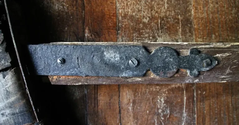 Close-up of a door hinge with loose screws on a wood sagging door