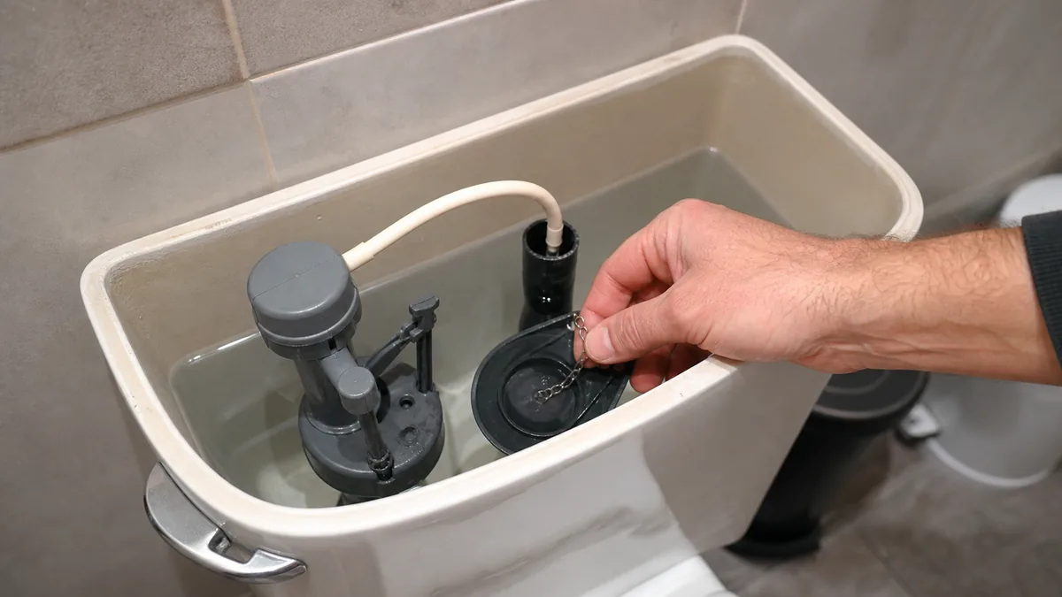 Open toilet tank showing a homeowner checking a flapper seal and lift chain