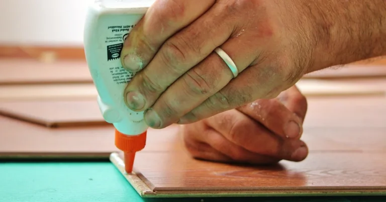 Hand applying wood glue to a tongue and groove flooring board