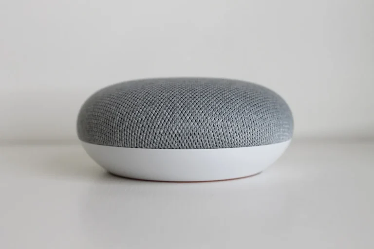 A person compares two smart speakers beside a smartphone in a modern living room.
