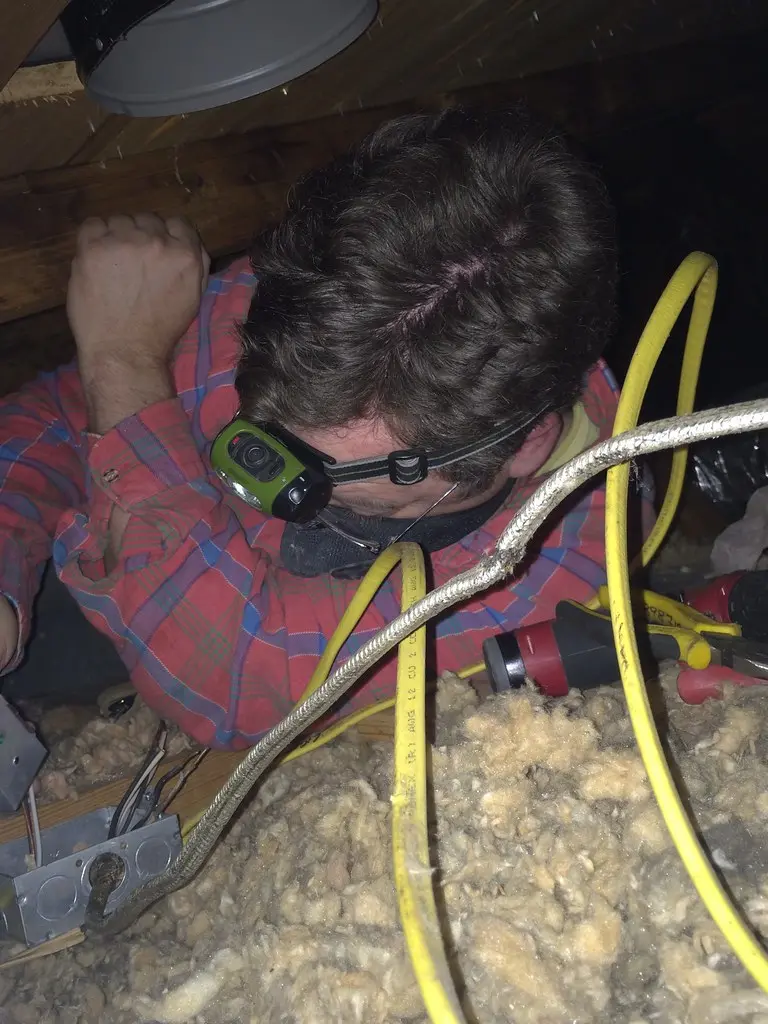 A homeowner compares two bathroom exhaust fans beside a bathroom vent opening.