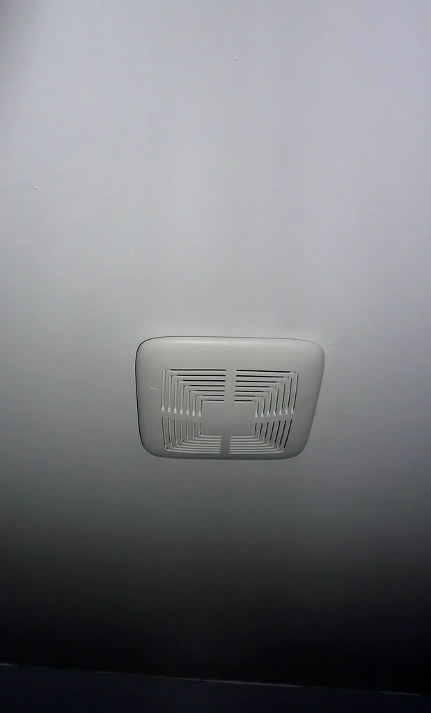 A close-up of a bathroom fan grille with an anemometer measuring airflow.