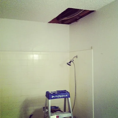 Hands applying fresh caulk along a bathtub edge beside tiled wall