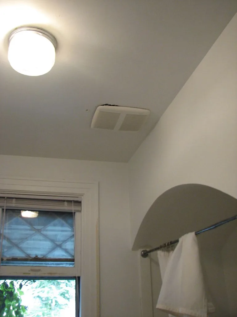 A bright bathroom with a ceiling ventilation fan above the shower and a homeowner assessing it