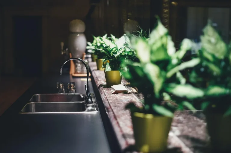 Modern stainless-steel faucet in a bright kitchen with visible water spots on nearby surfaces.