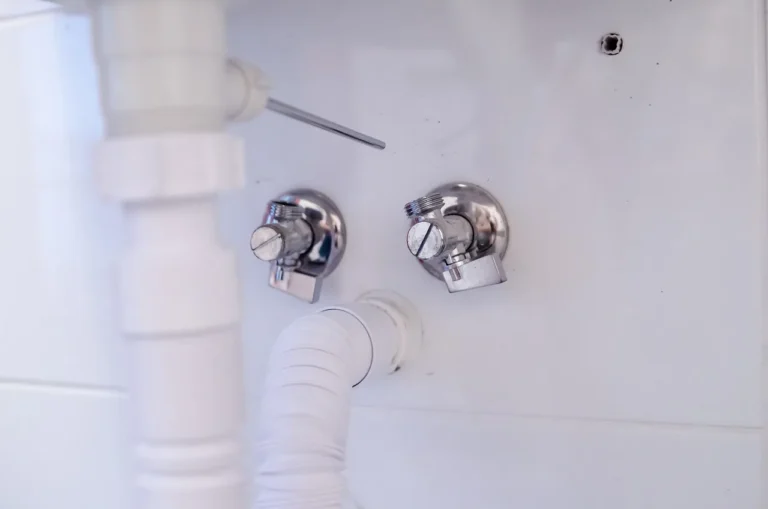 Plumber comparing a sink shutoff valve in a bathroom remodel beside open vanity plumbing