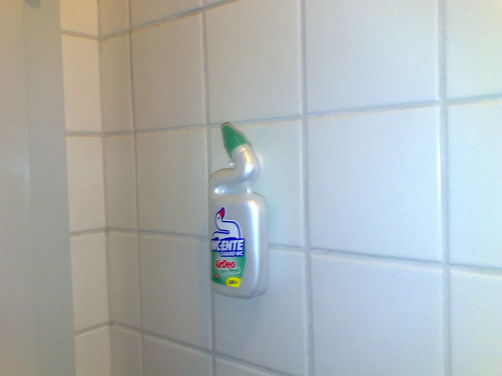 Gloved hand applying toilet bowl cleaner gel under the rim of a porcelain toilet