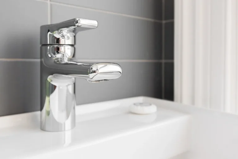 Brushed nickel and stainless steel faucet samples beside a bathroom sink in natural light
