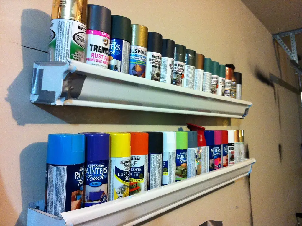 Close-up of a gloved hand spray painting a prepared drawer front after sanding and priming.