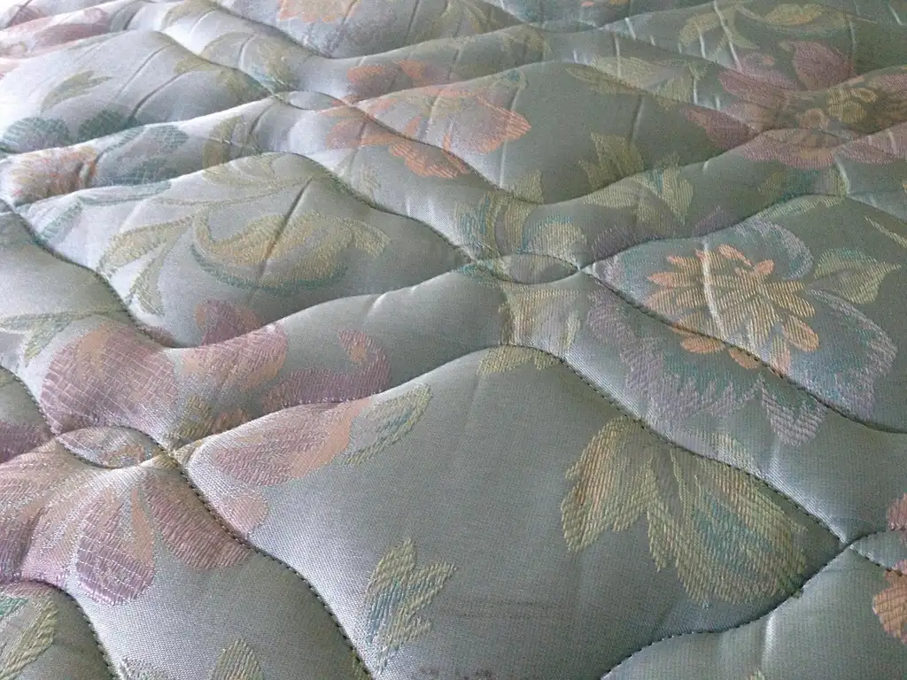 Adult testing a soft mattress by pressing it while sitting on the bed, looking concerned about back pain.