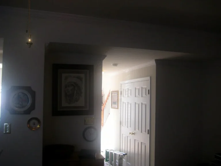 Crown molding being measured and test-fit in a bright living room with a step ladder