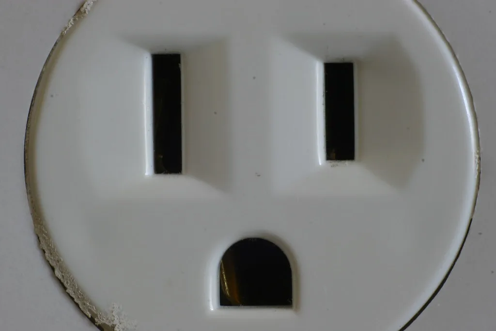 Electrician testing a GFCI outlet with a plug-in tester near a bathroom sink