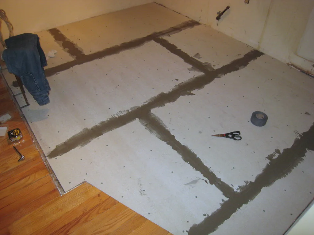 Hands sealing floor underlayment seams on a plywood subfloor