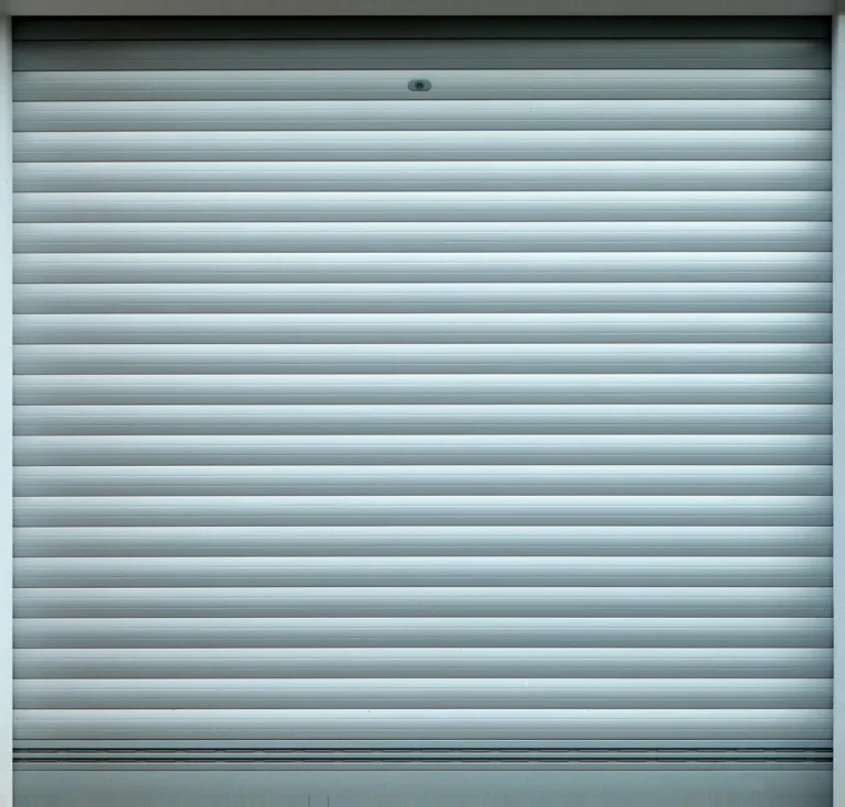 Garage door technician inspecting an overhead garage door beside a suburban home