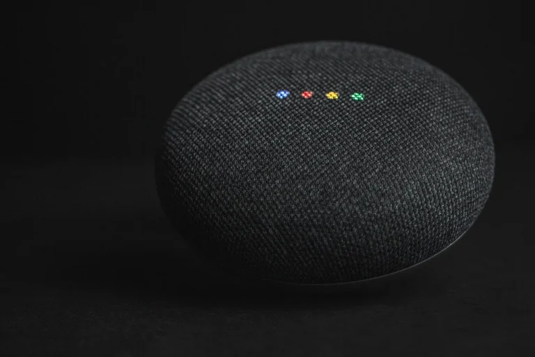 A homeowner compares a Google Home speaker with a laptop and several smart devices on a table