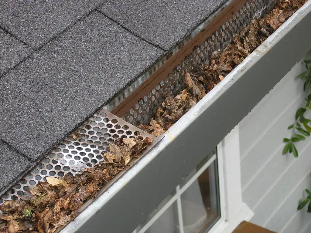 Homeowner inspecting rain gutters and a downspout beside a house with gutter accessory samples nearby