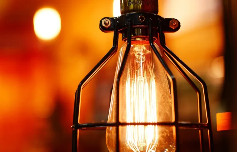 Close-up of a glowing light bulb in a black metal cage against a warm blurred background