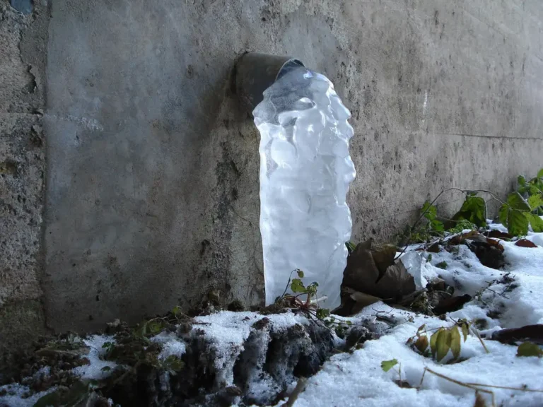 Homeowner inspects an exposed outdoor pipe run with frost on a freezing winter morning