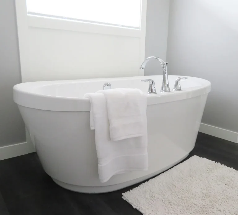 White freestanding bathtub with chrome faucet, towel draped over side, in a bright bathroom