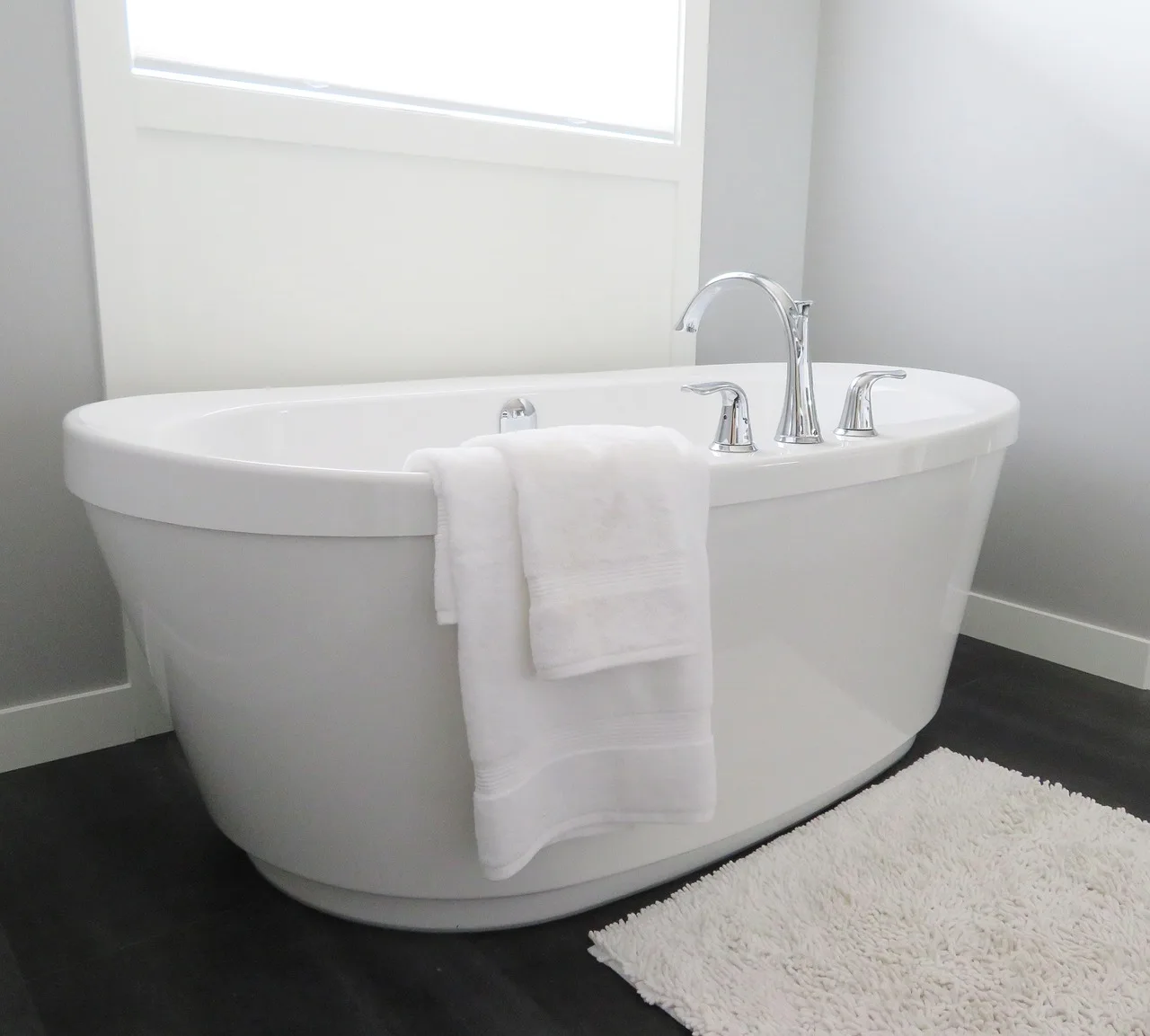 White freestanding bathtub with chrome faucet, towel draped over side, in a bright bathroom