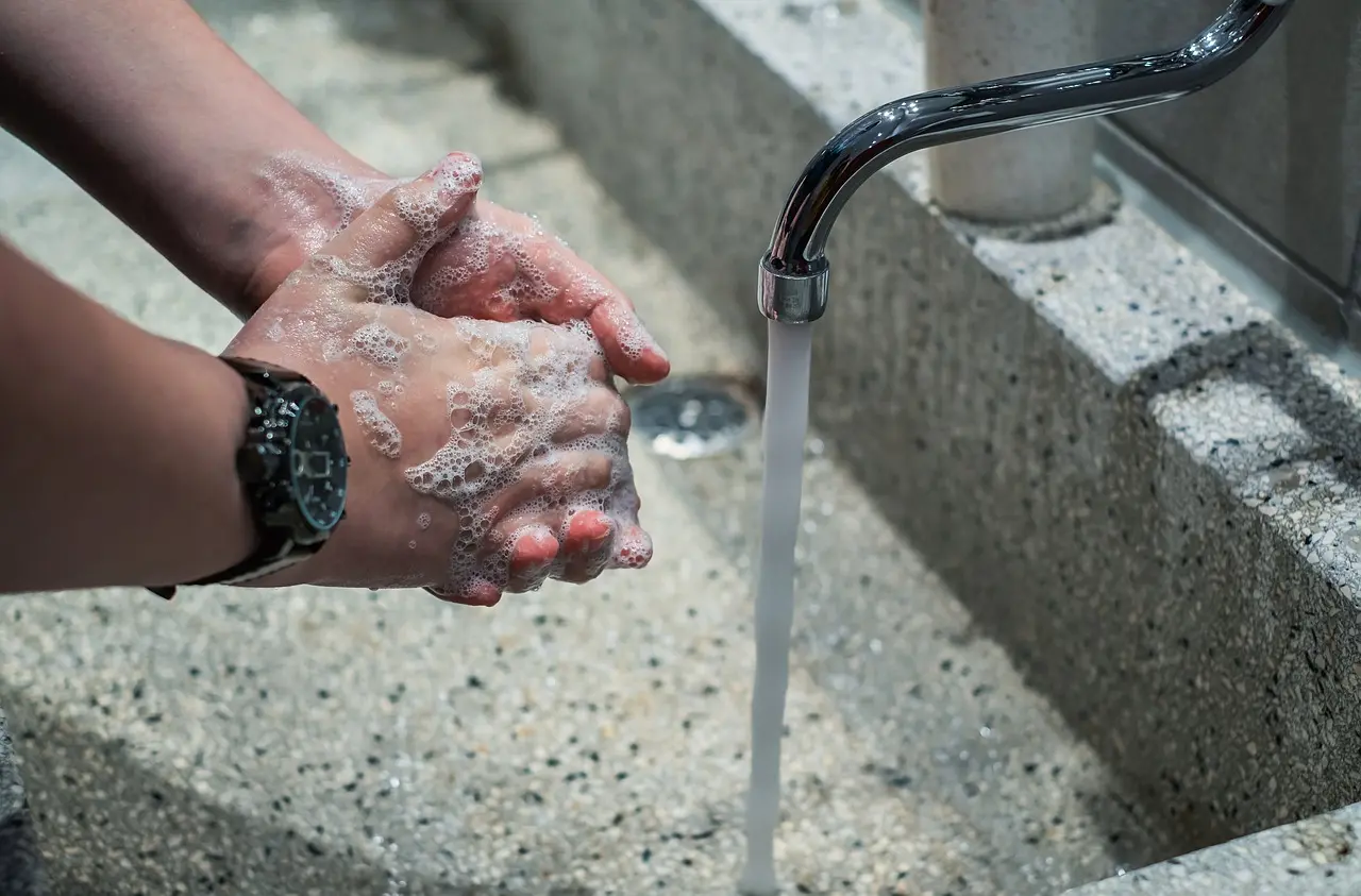 Hands covered in soap are washed under a running faucet at a sink