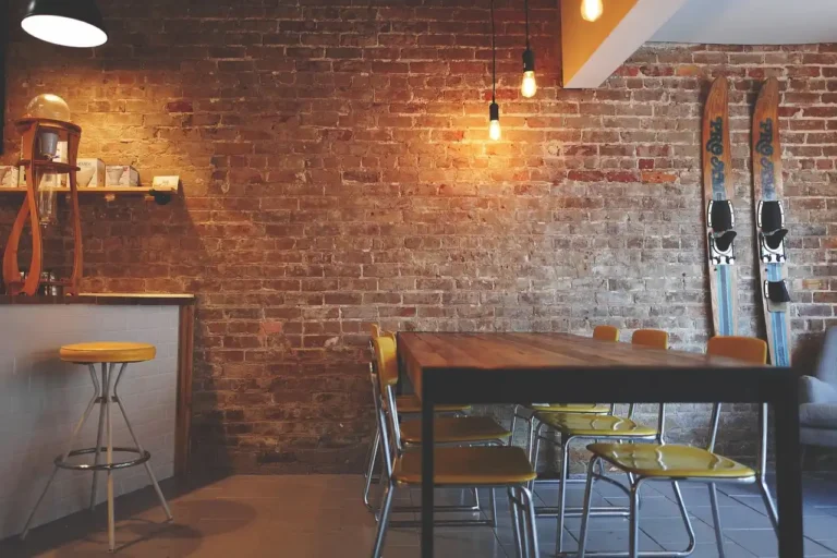 Brick-walled cafe with hanging lights, a wooden table, chairs, and skis on the wall