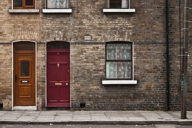Brick building facade with two front doors and a window along a sidewalk