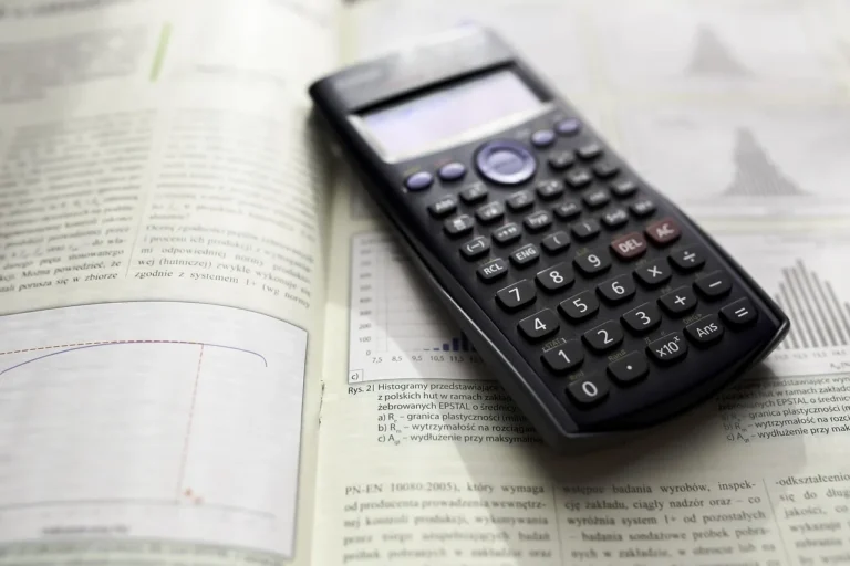A black scientific calculator rests on an open textbook displaying Polish text, graphs, and histograms