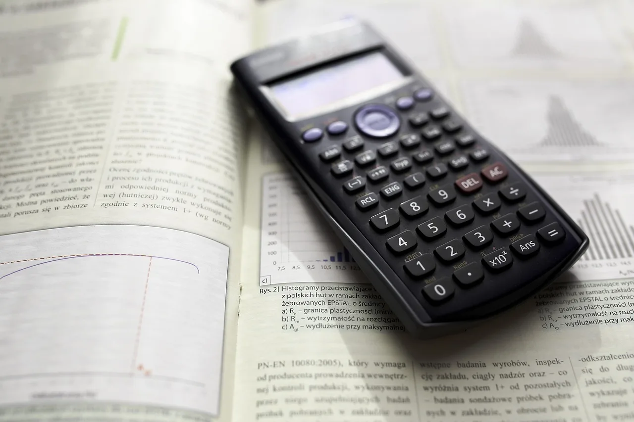 A black scientific calculator rests on an open textbook displaying Polish text, graphs, and histograms