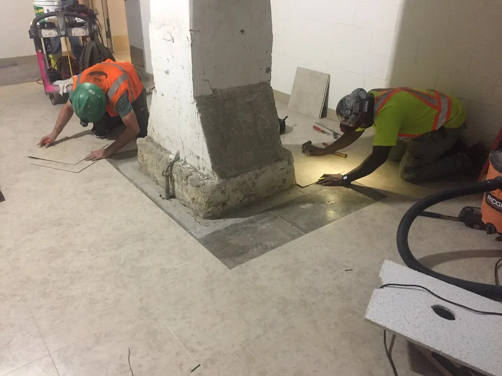 Hands unrolling roll of vinyl flooring and aligning it to the wall edge