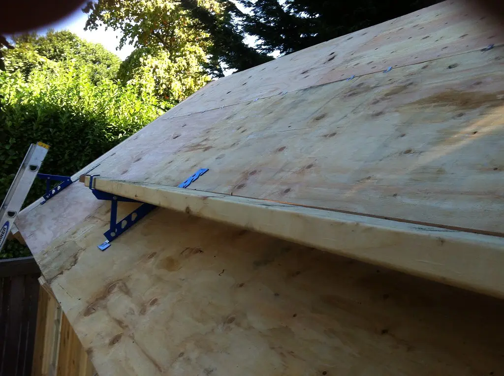 Hands marking an OSB roof sheathing panel with a tape measure and pencil