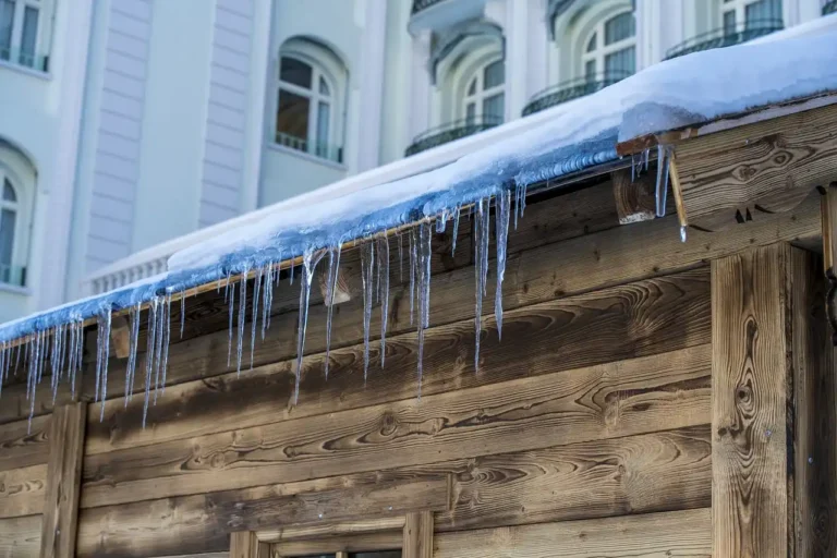 Ice dams lining a snowy roof edge on a house in winter daylight