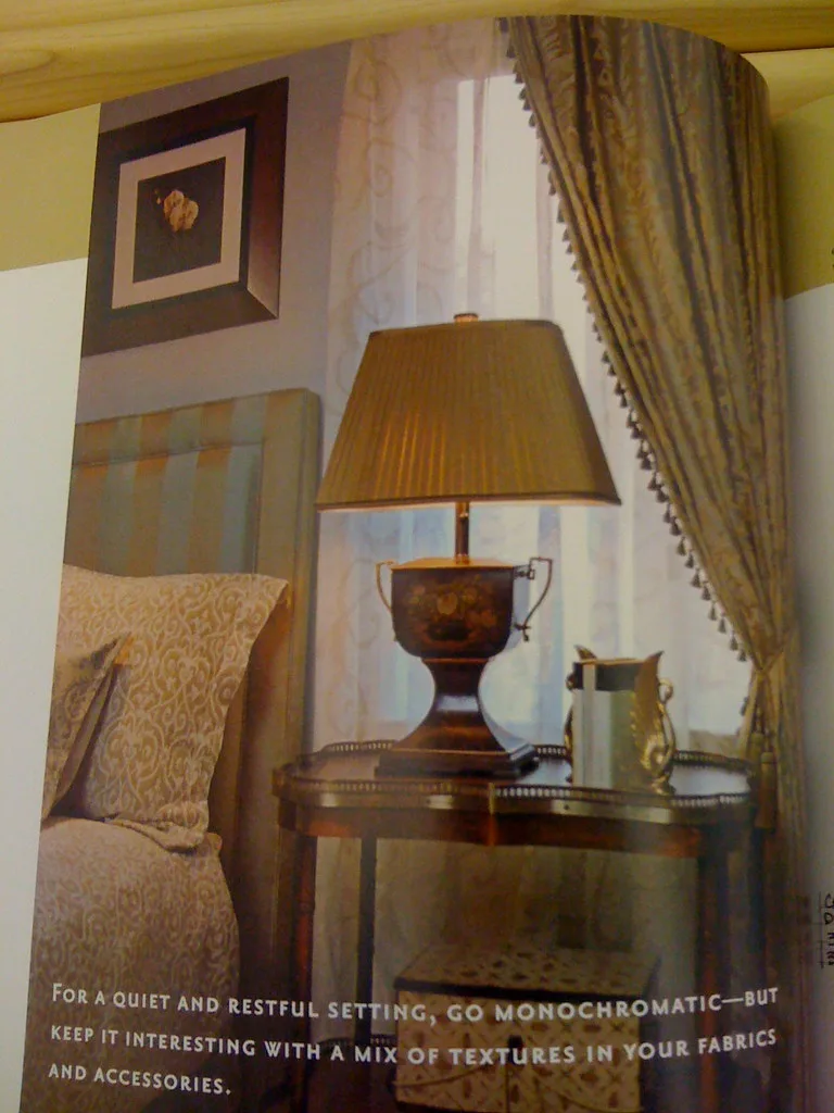 A bedside lamp with a warm bulb on a nightstand next to a book and sleeping mask.
