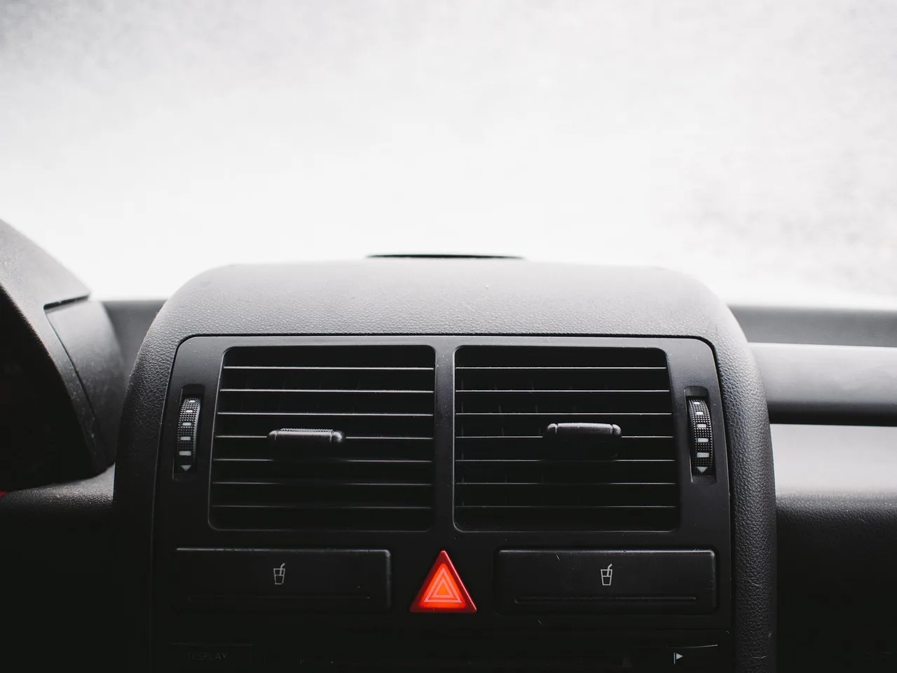 Car dashboard with two air vents and a lit red hazard light button below them