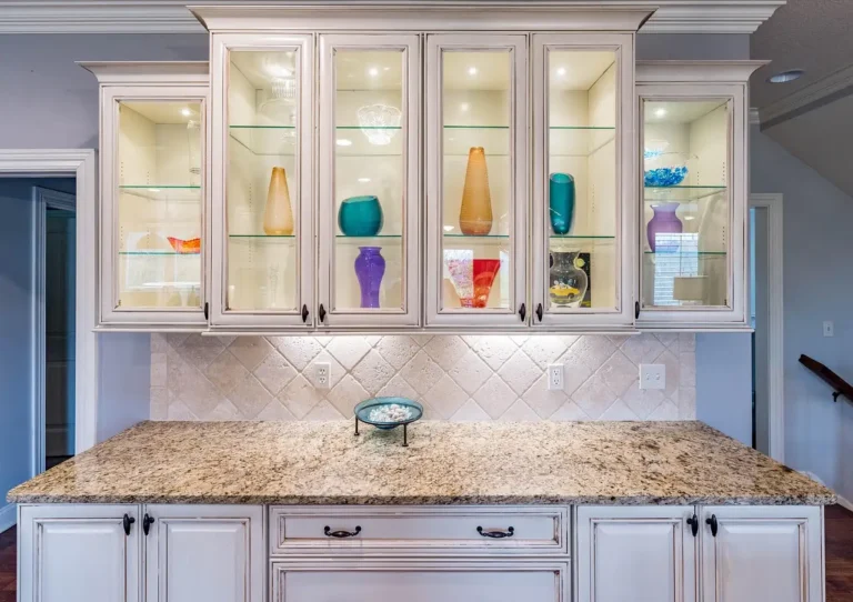 White kitchen cabinets with glass doors, lit shelves, and a granite countertop