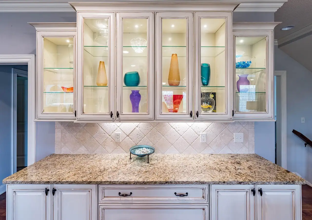 White kitchen cabinets with glass doors, lit shelves, and a granite countertop