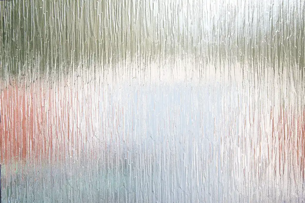 Homeowner beside a bedroom window with frost on the inside glass in winter light
