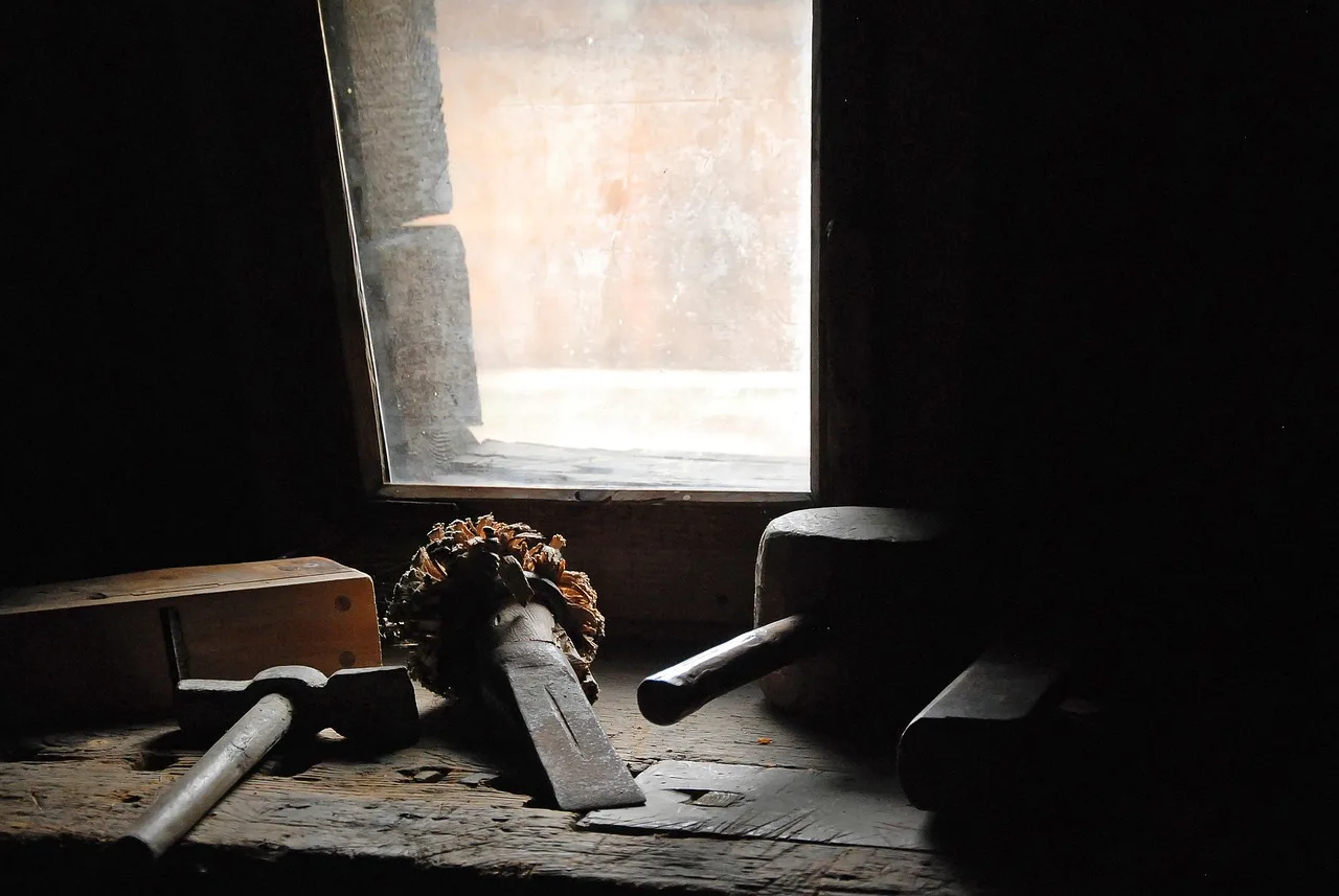 Woodworker reviewing tool costs beside a benchtop planer and laptop in a sunlit workshop